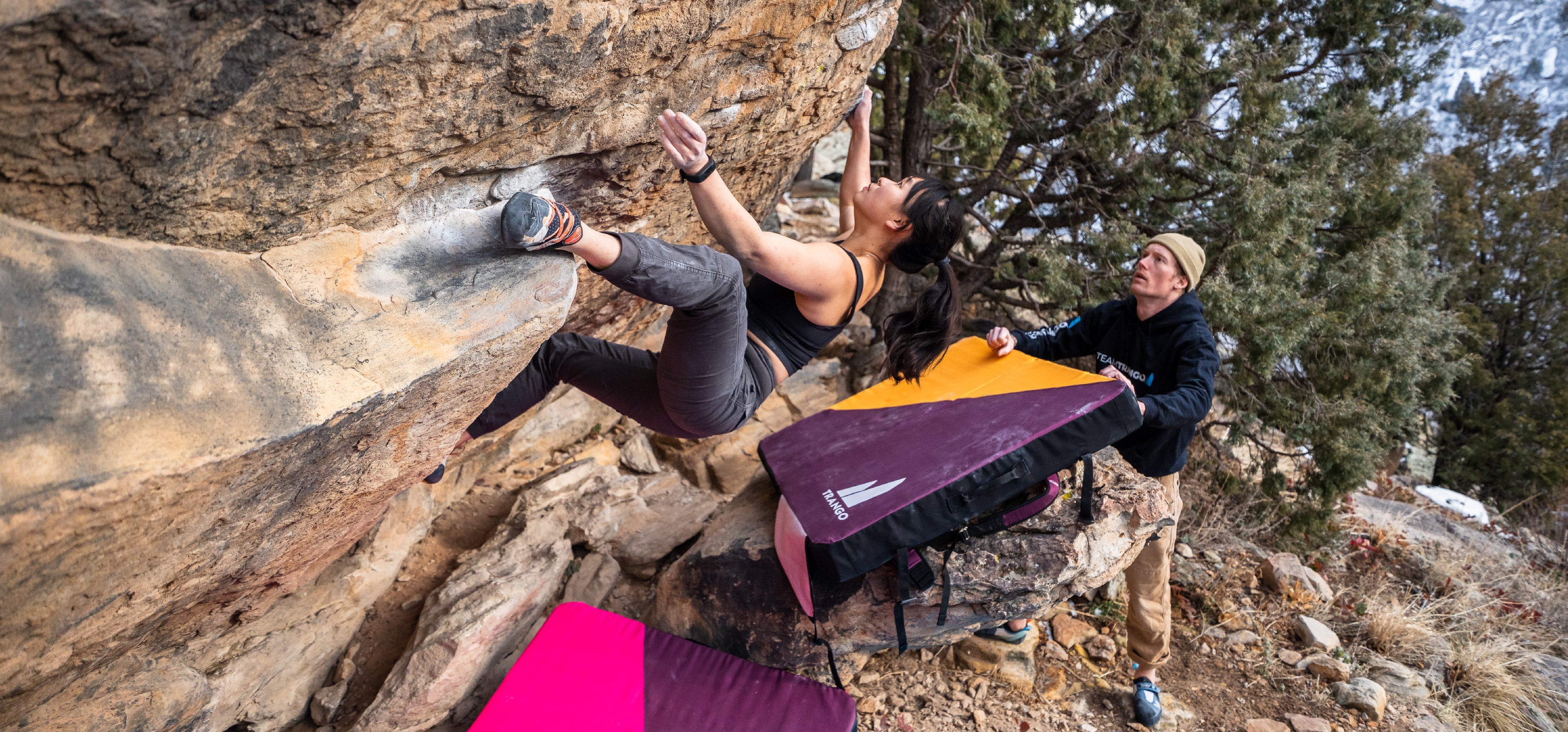 Person bouldering outdoors with another person positioning a Cumulus crashpad